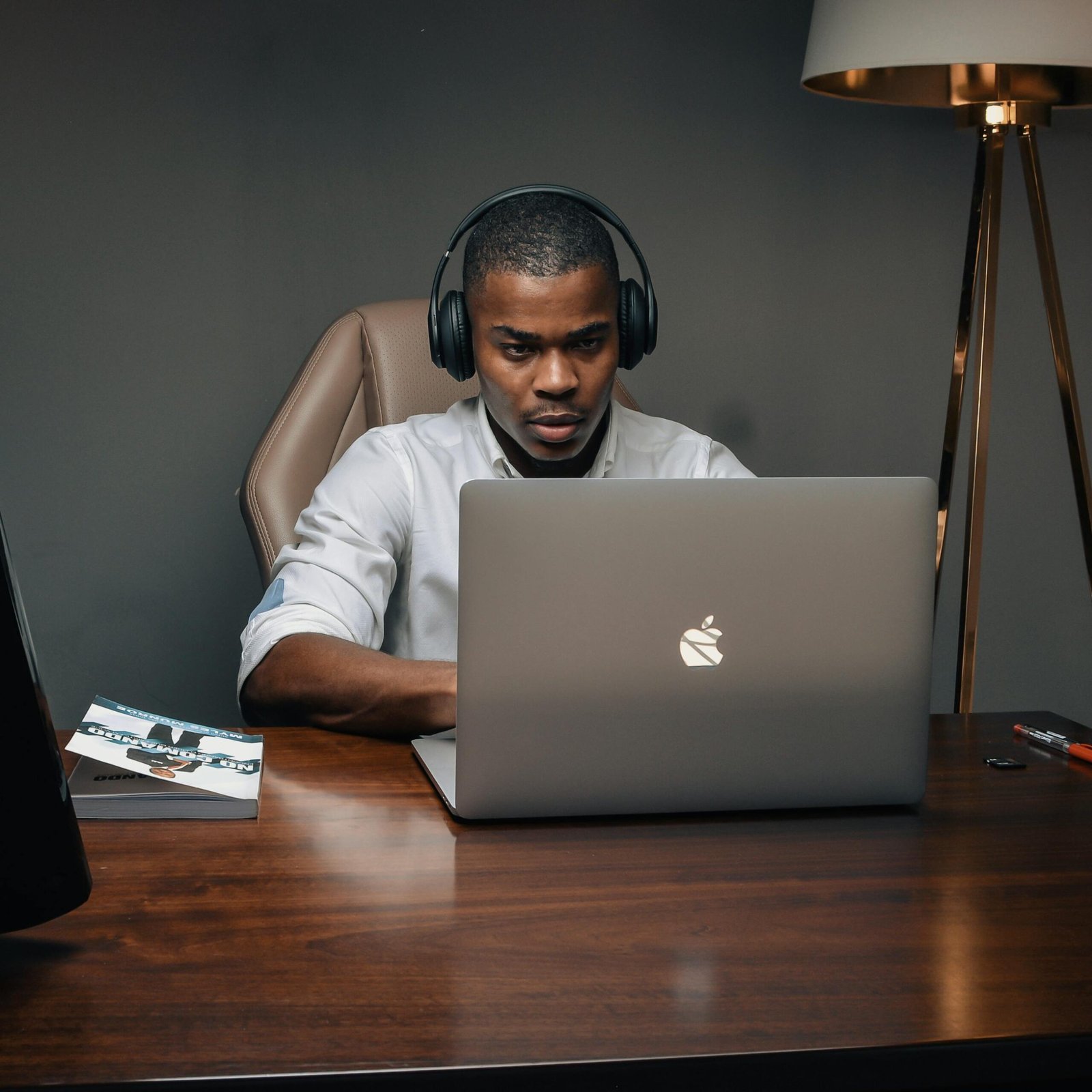 Professional man wearing headphones, working intently on a laptop in a modern office setting.