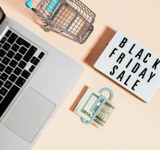 Overhead view of shopping cart, laptop, cash, and Black Friday sale sign.