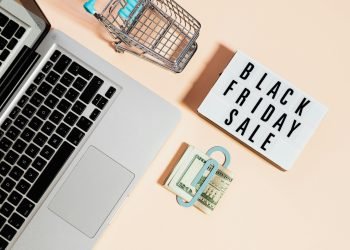 Overhead view of shopping cart, laptop, cash, and Black Friday sale sign.