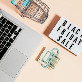 Overhead view of shopping cart, laptop, cash, and Black Friday sale sign.