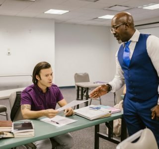 A teacher and student engaged in a discussion over an exam paper in a classroom setting.