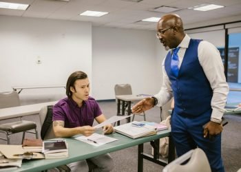 A teacher and student engaged in a discussion over an exam paper in a classroom setting.