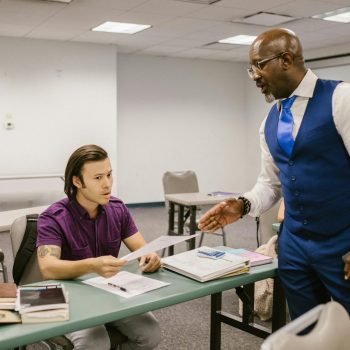 A teacher and student engaged in a discussion over an exam paper in a classroom setting.