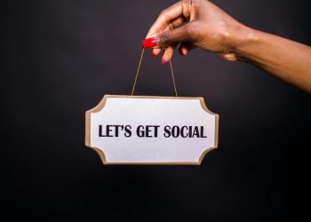 Close-up of a hand holding a sign with 'Let's Get Social' on a dark background.