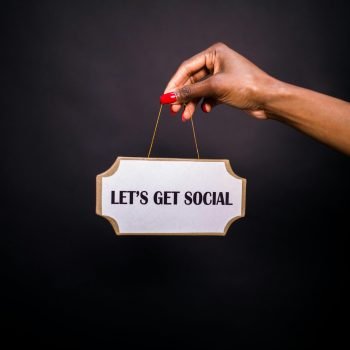 Close-up of a hand holding a sign with 'Let's Get Social' on a dark background.