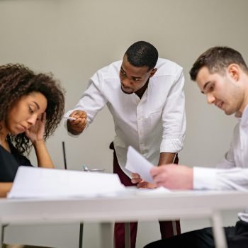 A diverse team engaged in a serious office discussion around a table, focusing on documents.